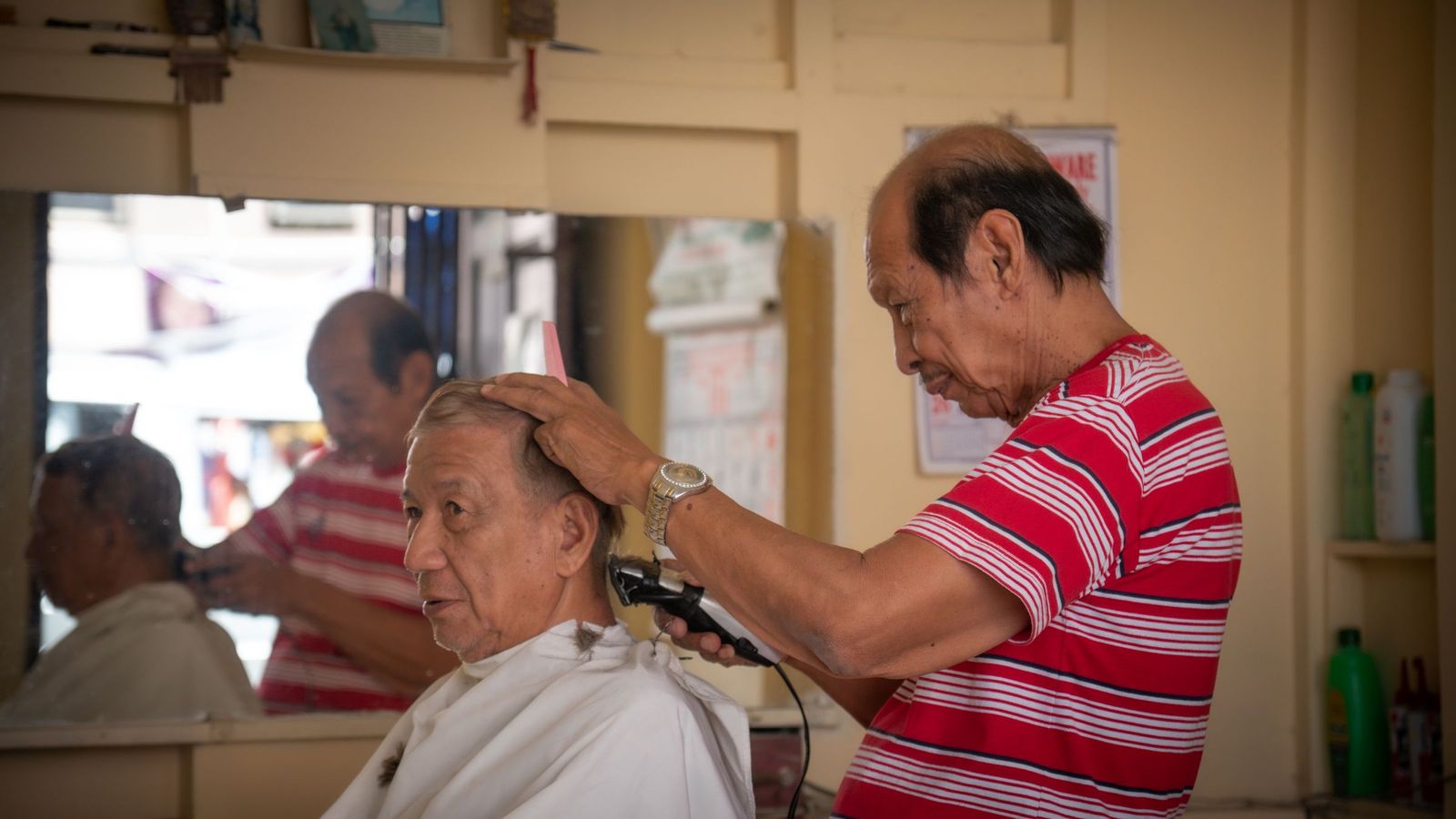 ช่างตัดผมชายใช้ปัตตาเลี่ยนตัดแต่งผมให้ลูกค้าในร้านบาร์เบอร์ที่มีแสงแดดส่องเข้ามาสว่างทั่วร้าน