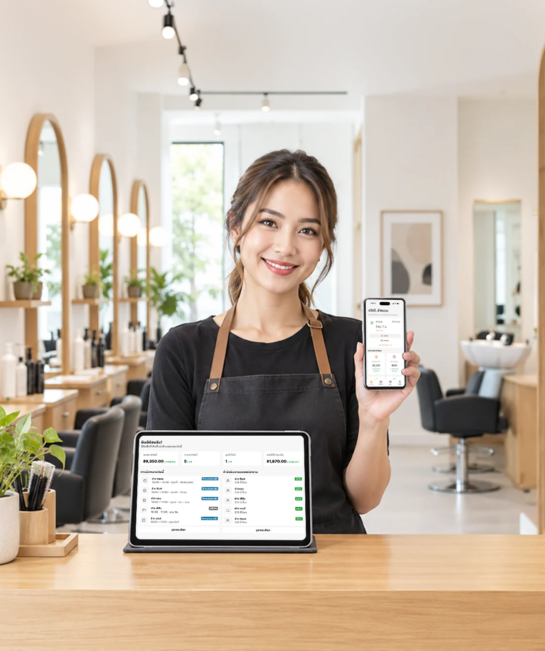เจ้าของร้านเสริมสวยยืนที่เคาน์เตอร์ ถือมือถือที่เปิดแอป SalonX และมีแท็บเล็ตแสดงสรุปยอดขายและงานของทีมช่างวางอยู่ด้านหน้า